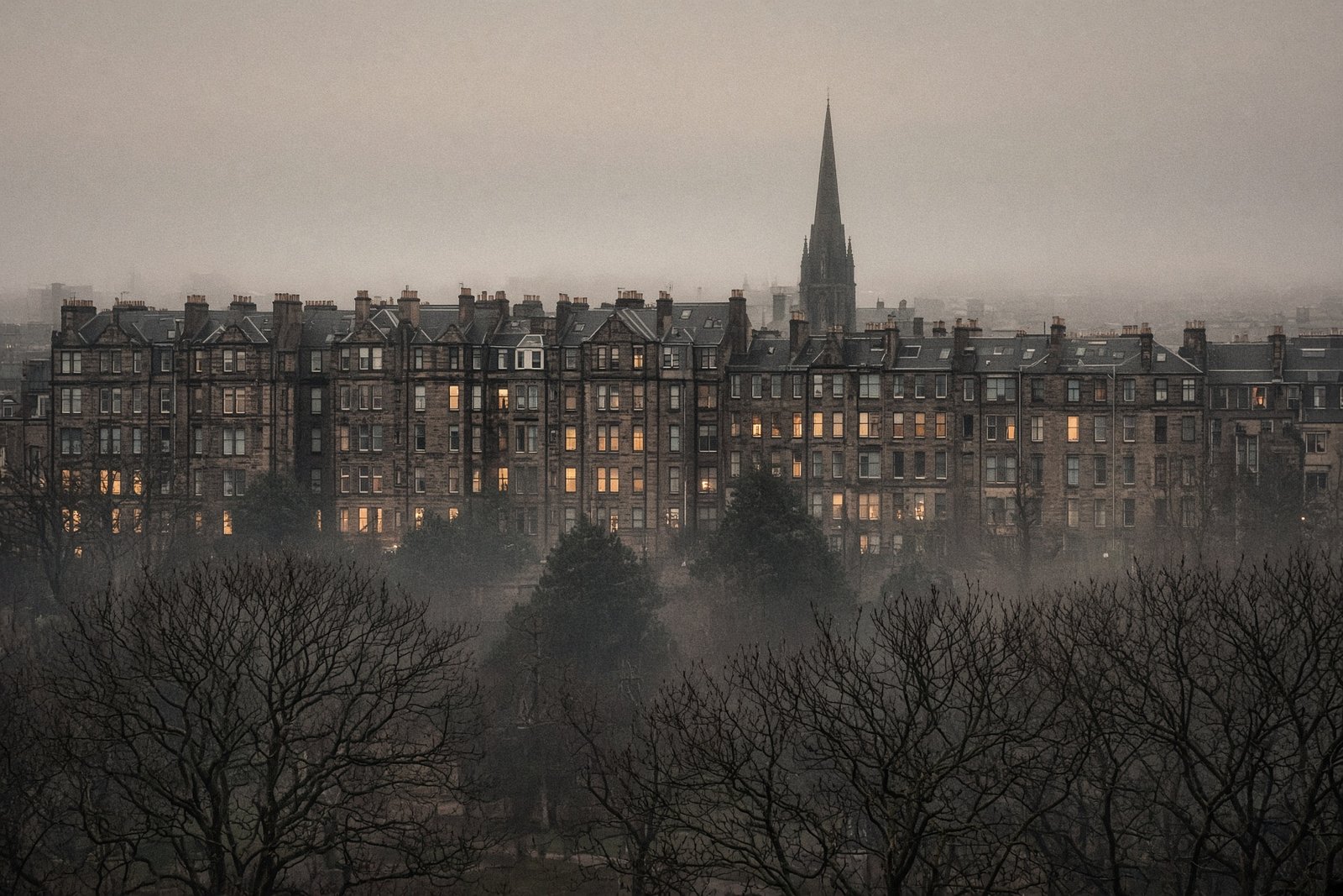Stone city seen across bare trees in thin mist, with a distant spire
