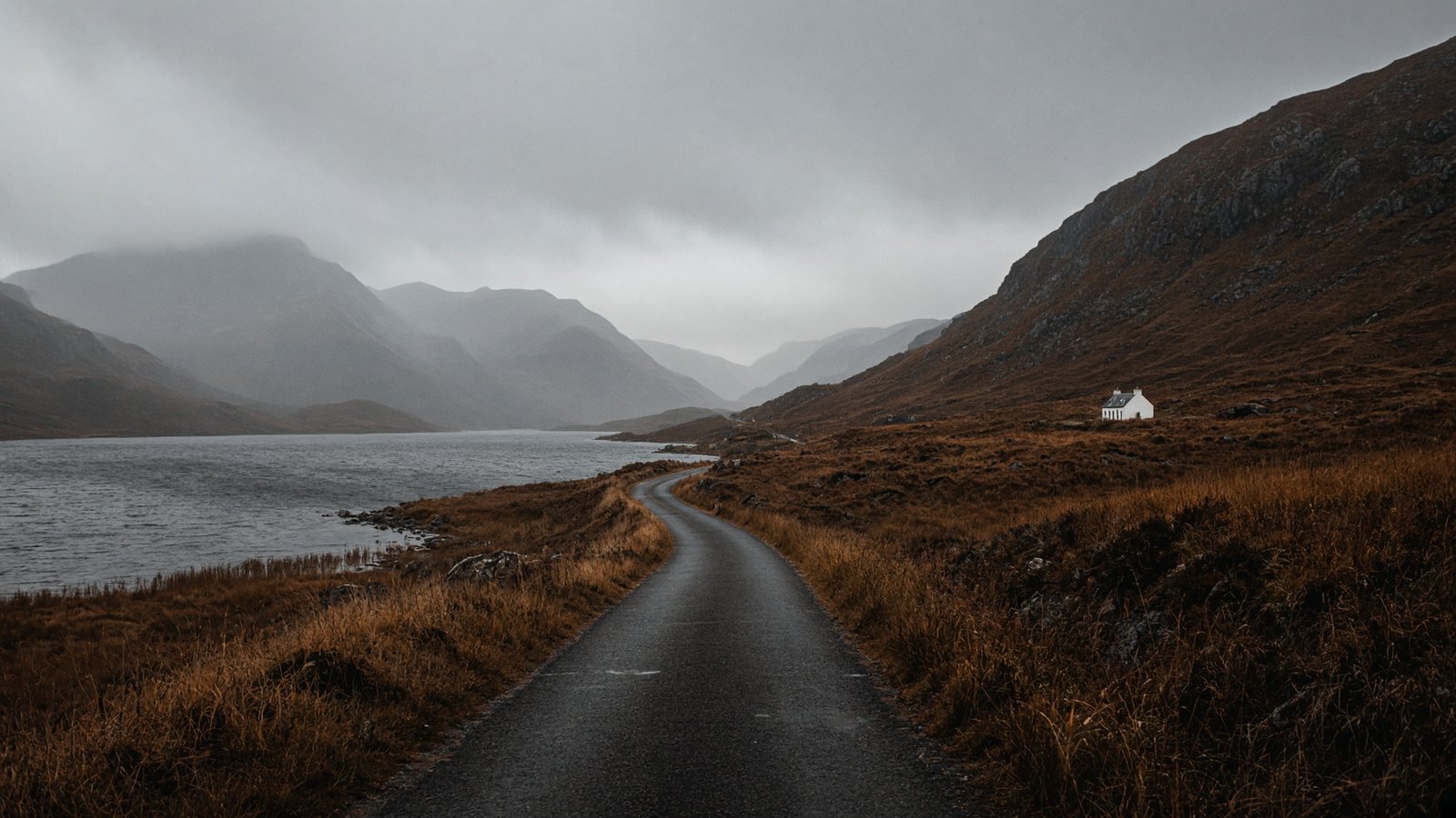 Single-track road beside a dark loch in a rainy Highland glen