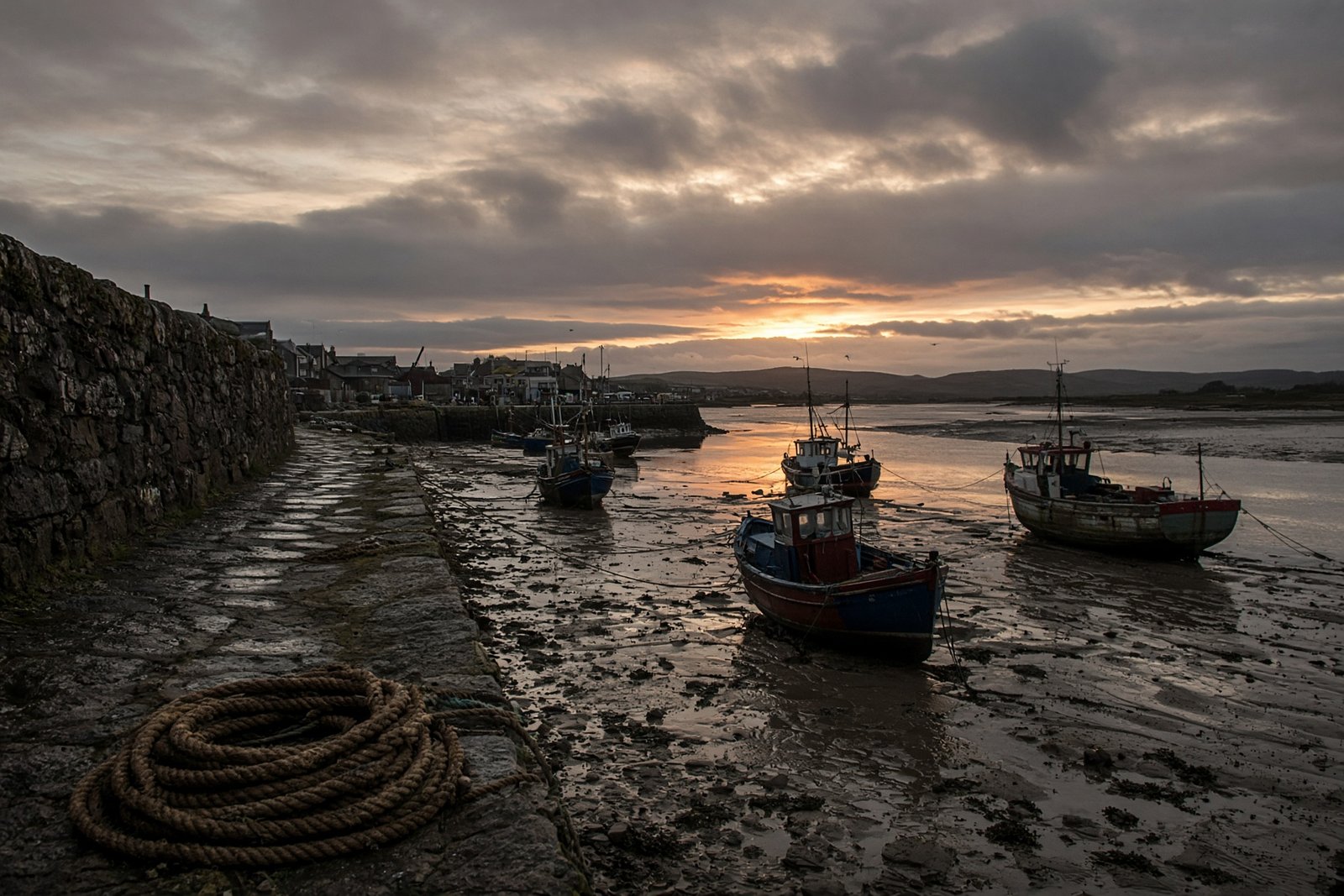 Stone fishing harbour at low tide with working boats and a low sun